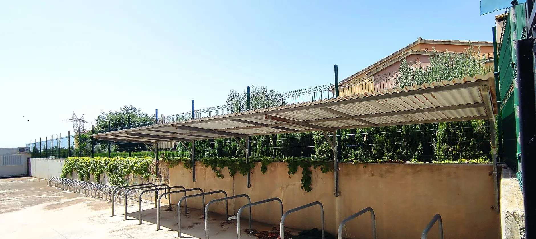 Hilera de aparcabicis de acero bajo una cubierta junto a un muro