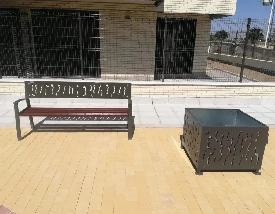Banco de madera y acero con respaldo perforado junto a una jardinera a juego