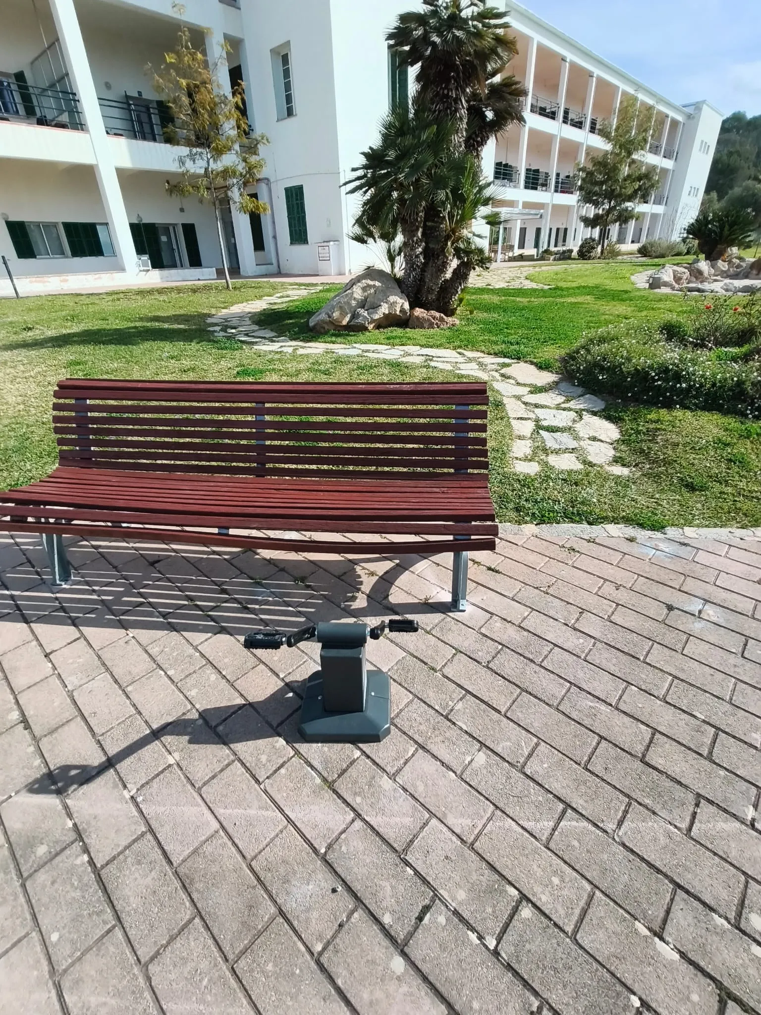 Banco de madera y metal en un paseo adoquinado junto a un jardín