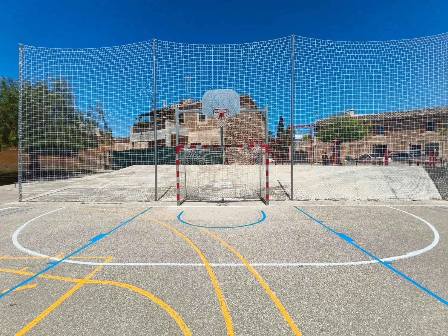Portería y canasta de una pista multideporte con marcaje de varios deportes y red de protección