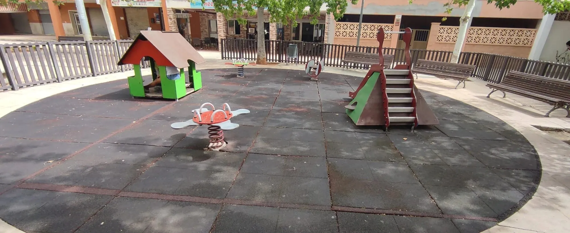 Parque infantil con el pavimento de caucho negro desgastado antes de la renovación