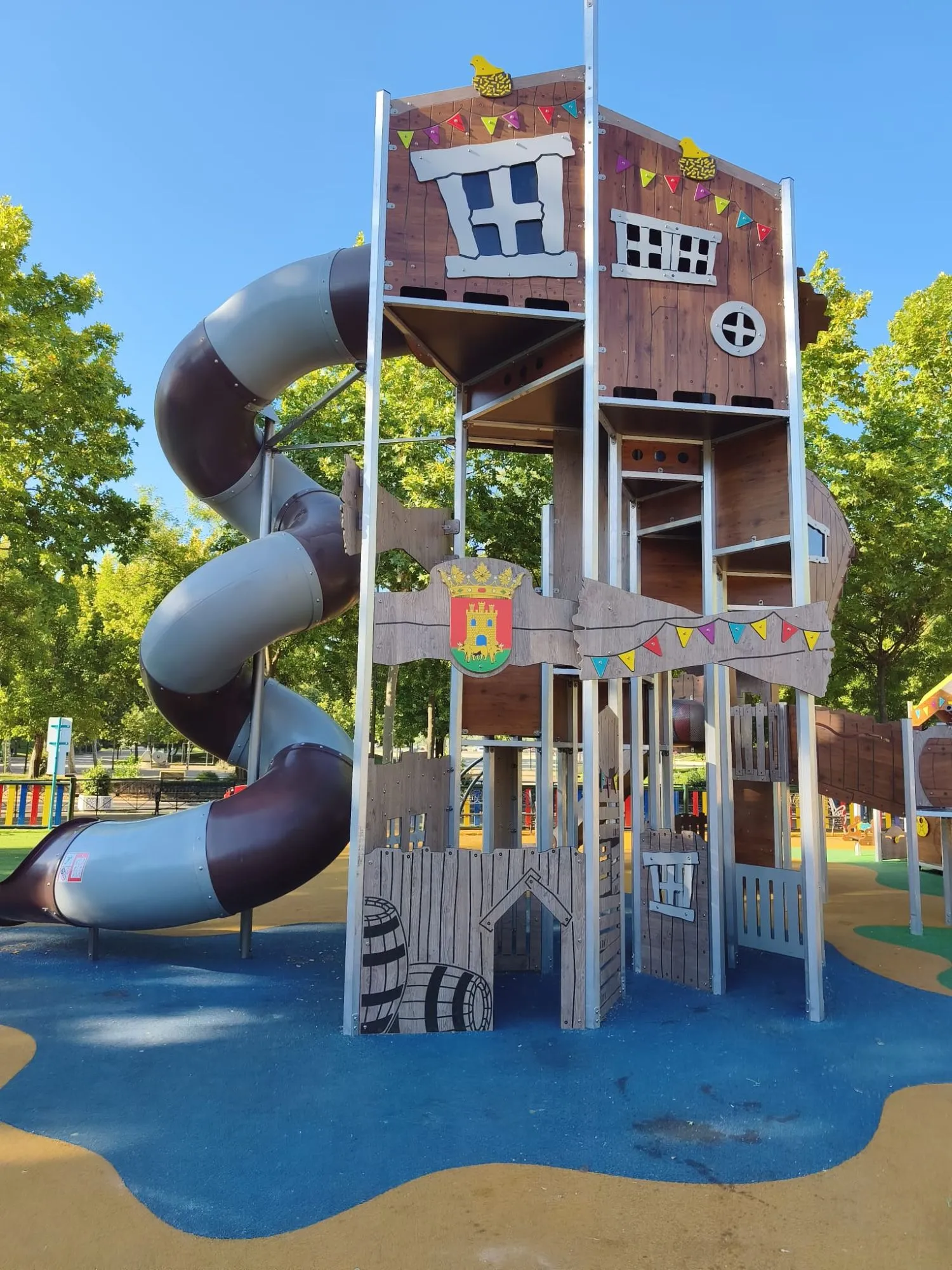 Torre de juego temática de madera con tobogán tubular en espiral sobre pavimento de caucho azul